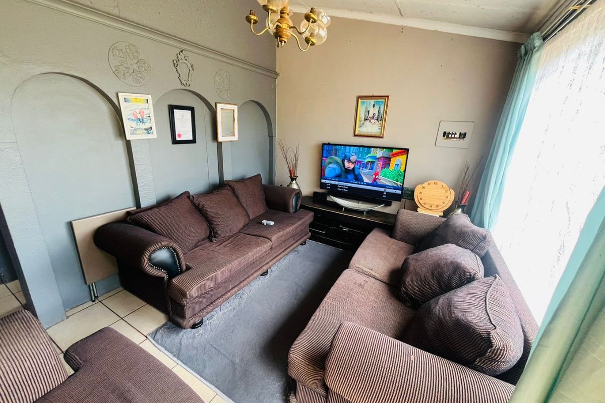 A living room featuring decorative wall arches, tiled flooring, and a central chandelier, offering a dated aesthetic ready for modernization.