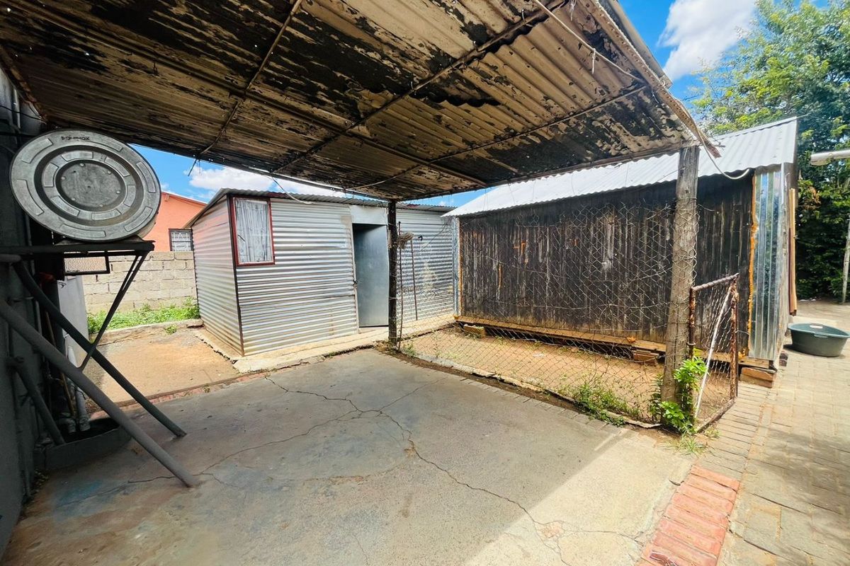 Rear yard area featuring a weathered corrugated iron roof structure, concrete paving, and multiple outbuildings with visible signs of wear and structural aging.