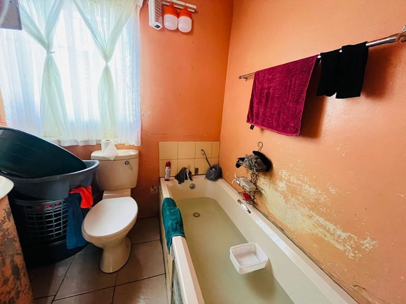 A dated bathroom featuring a standard bathtub and toilet, requiring cosmetic updates and wall repairs to improve the overall condition and aesthetic appeal.