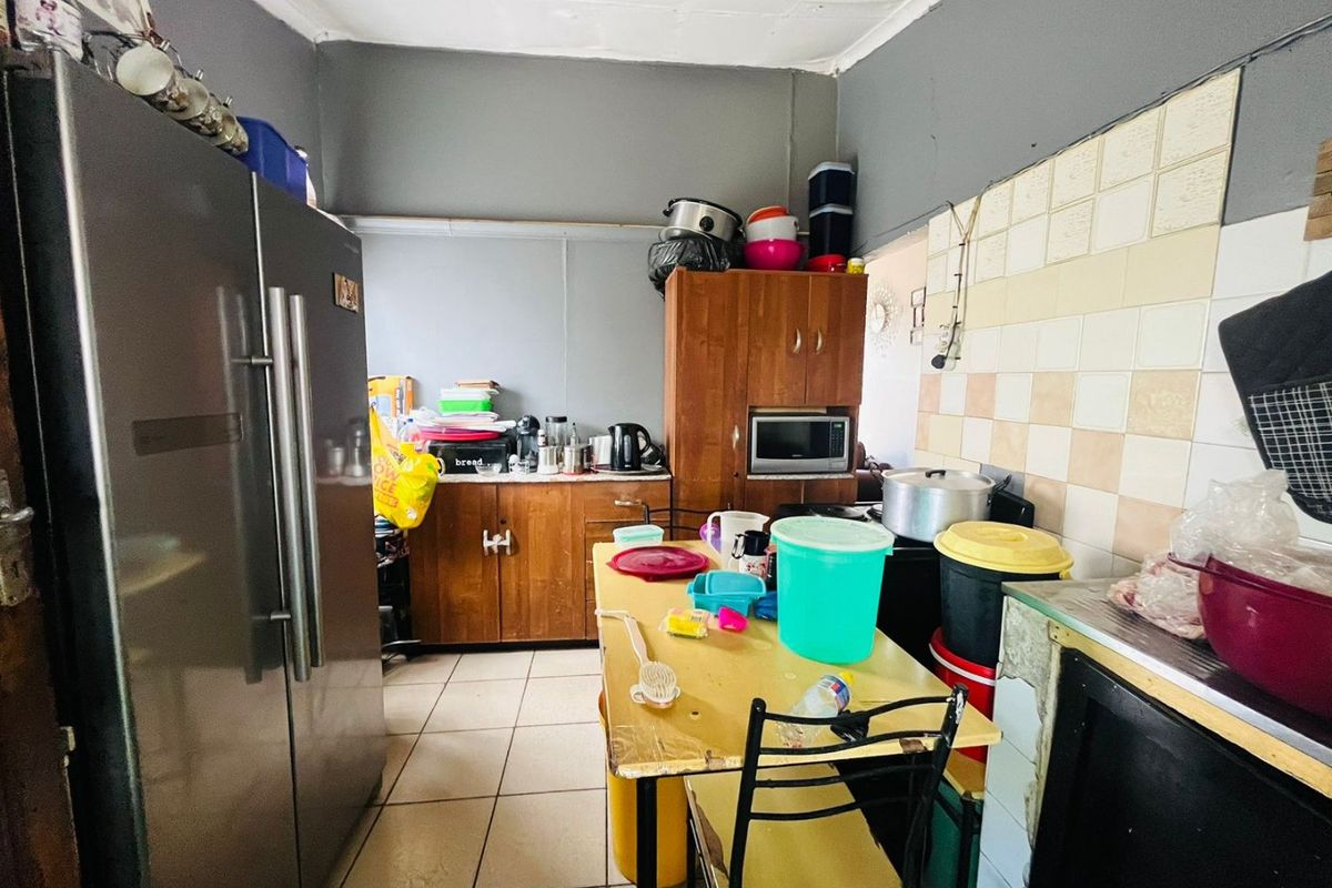 A functional kitchen space featuring tiled flooring, a tiled splashback, and built-in wooden cabinetry, offering potential for modernization and layout optimization.