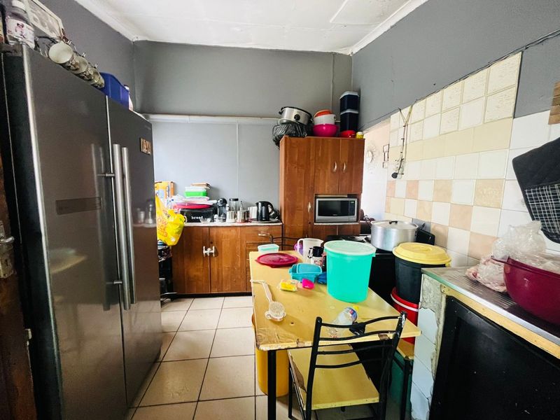 A functional kitchen space featuring tiled flooring, a tiled splashback, and built-in wooden cabinetry, offering potential for modernization and layout optimization.