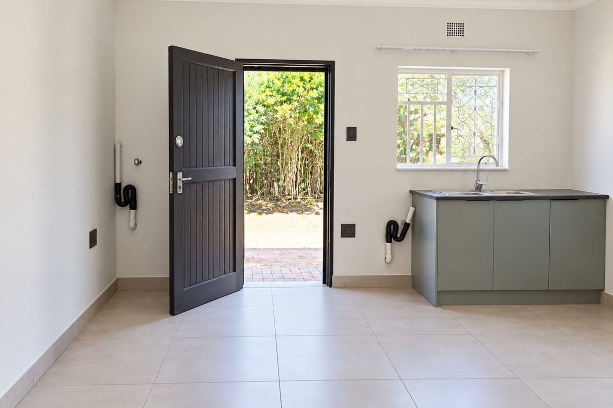 A clean, modern laundry room featuring tiled floors, built-in cabinetry with a sink, and direct access to the garden through a secure door.