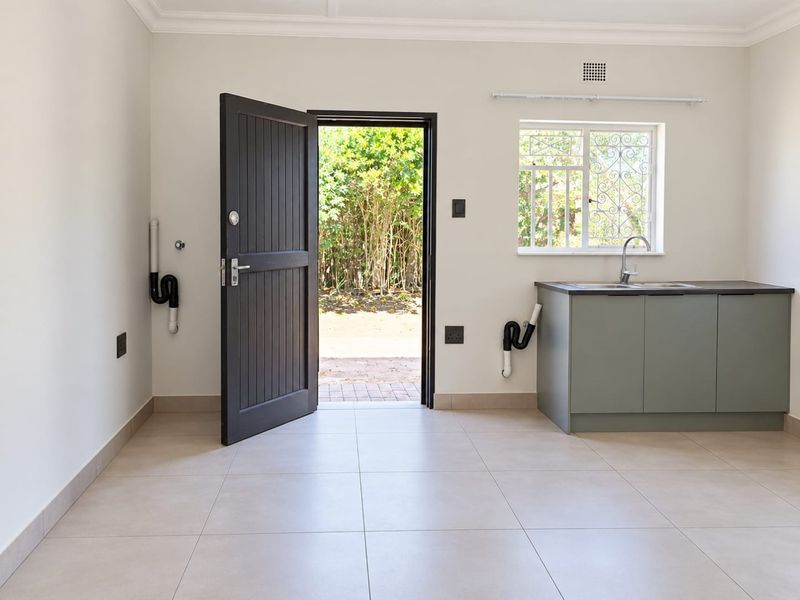 A clean, modern laundry room featuring tiled floors, built-in cabinetry with a sink, and direct access to the garden through a secure door.