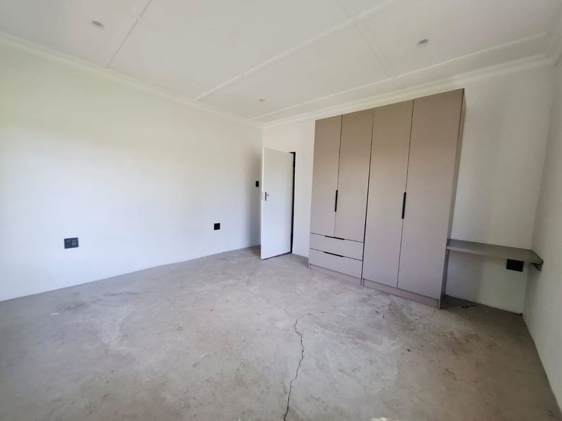 An empty bedroom featuring built-in cupboards with an integrated desk, recessed lighting, and a concrete floor requiring finishing.