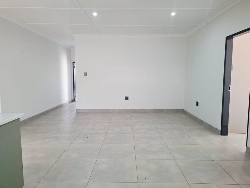 A bright, empty living area featuring neutral tiled flooring, clean white walls, and modern recessed downlighting, providing a versatile blank canvas for interior design.