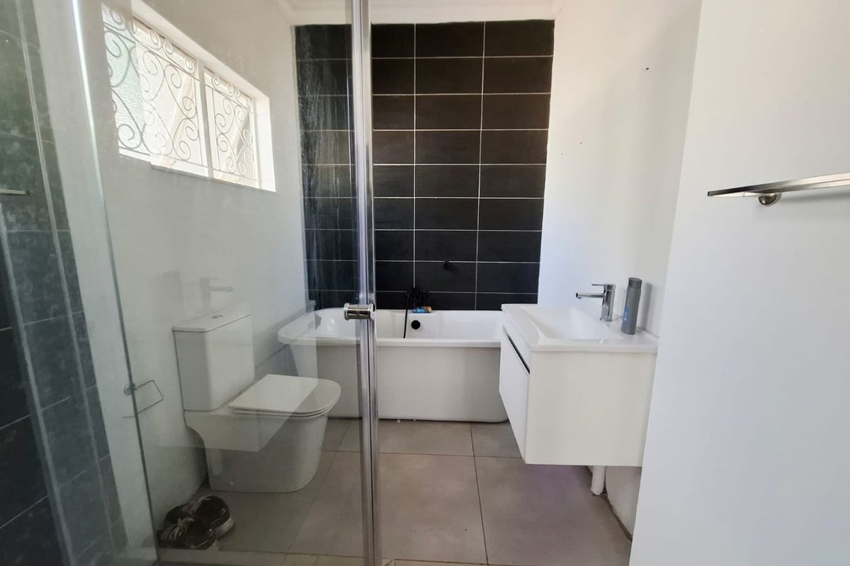 Modern bathroom featuring a freestanding bathtub, wall-mounted vanity, glass shower enclosure, and contrasting dark tiled feature wall.