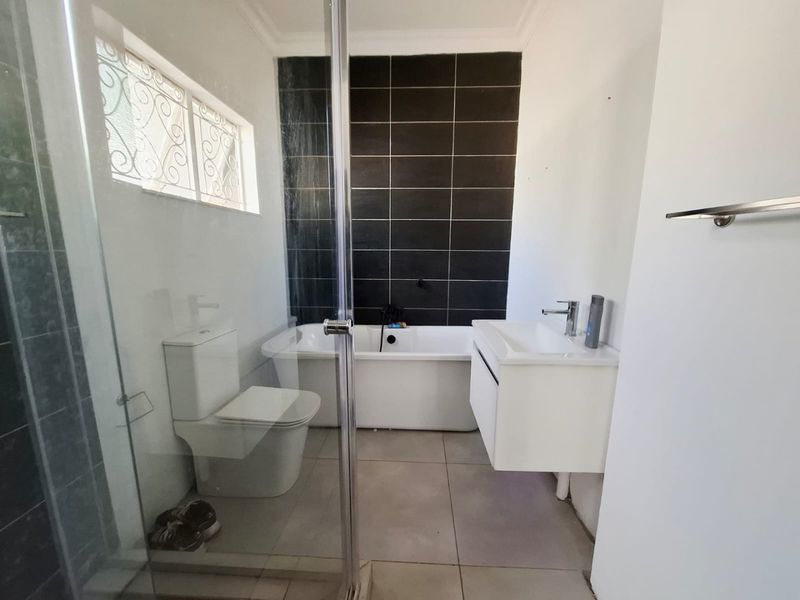 Modern bathroom featuring a freestanding bathtub, wall-mounted vanity, glass shower enclosure, and contrasting dark tiled feature wall.