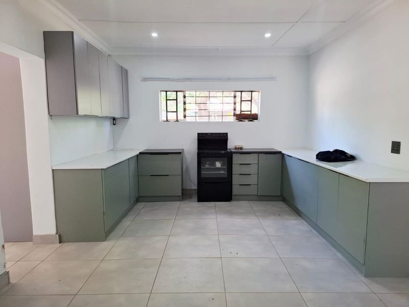 A clean, modern kitchen featuring sage green cabinetry, white countertops, tiled flooring, and a built-in oven, offering a functional and bright workspace.