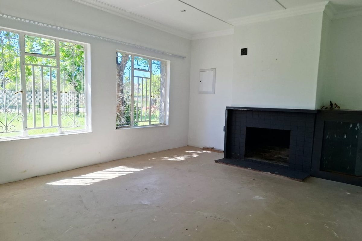 An empty living room featuring a black tiled fireplace, large windows with security bars, and unfinished flooring, offering a blank canvas for renovation.