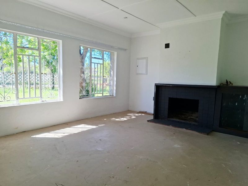 An empty living room featuring a black tiled fireplace, large windows with security bars, and unfinished flooring, offering a blank canvas for renovation.