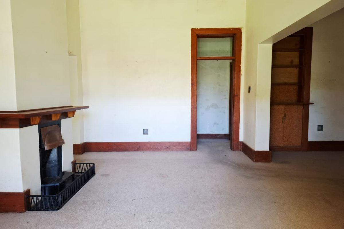 Spacious living room featuring a traditional fireplace with timber mantelpiece, built-in shelving, and original timber trim details, ready for renovation.