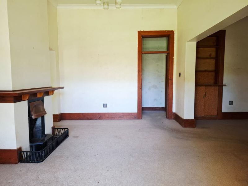 Spacious living room featuring a traditional fireplace with timber mantelpiece, built-in shelving, and original timber trim details, ready for renovation.