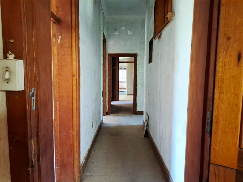 A long, narrow hallway featuring original timber door frames and skirting boards, currently in need of cosmetic renovation and wall surface repairs.