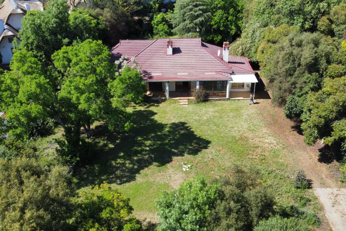 Aerial view of a residential property featuring a large garden, mature trees, and a house with a tiled roof and patio area.