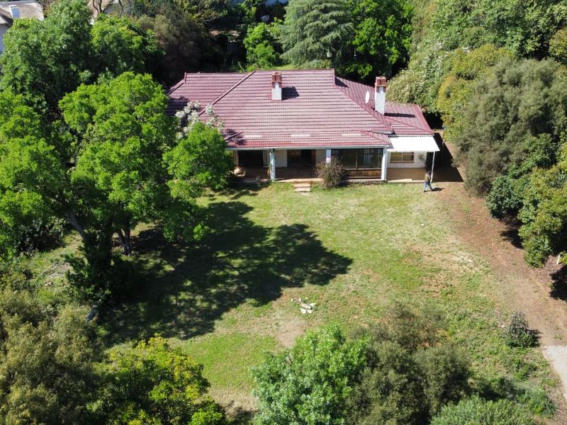 Aerial view of a residential property featuring a large garden, mature trees, and a house with a tiled roof and patio area.