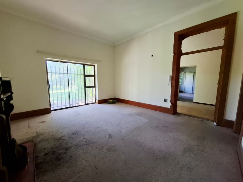 An empty living room featuring a fireplace, sliding glass door with security bars, and original timber door frames, requiring cosmetic updates and flooring replacement.