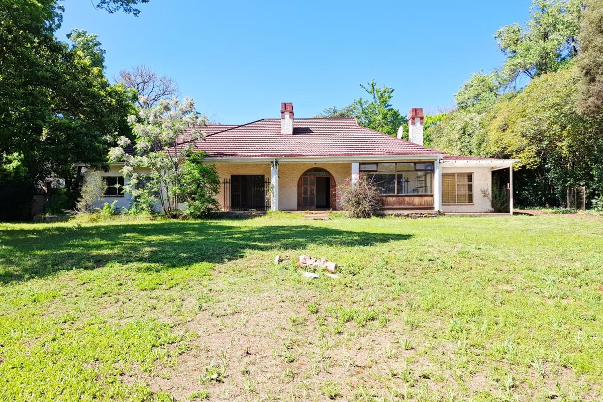 Rear view of a single-story house featuring a tiled roof, brick chimneys, and a spacious garden with a covered patio area.