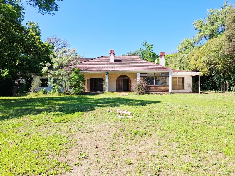 Rear view of a single-story house featuring a tiled roof, brick chimneys, and a spacious garden with a covered patio area.