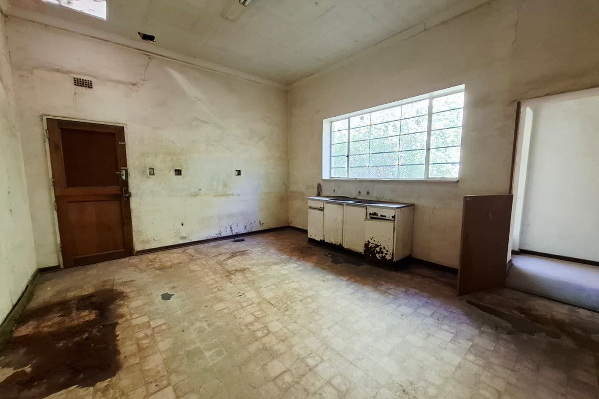 A vacant, original-condition kitchen space requiring significant renovation, featuring a basic sink unit, vinyl flooring, and dated wall finishes.