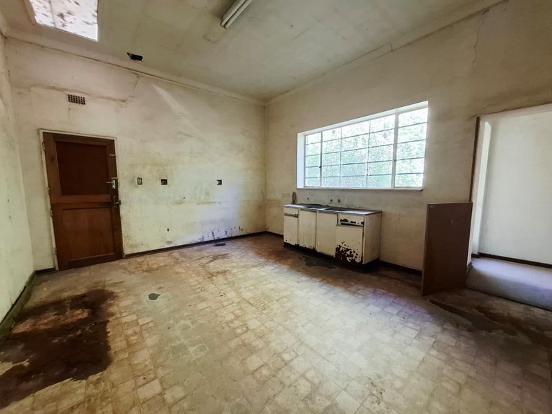 A vacant, original-condition kitchen space requiring significant renovation, featuring a basic sink unit, vinyl flooring, and dated wall finishes.