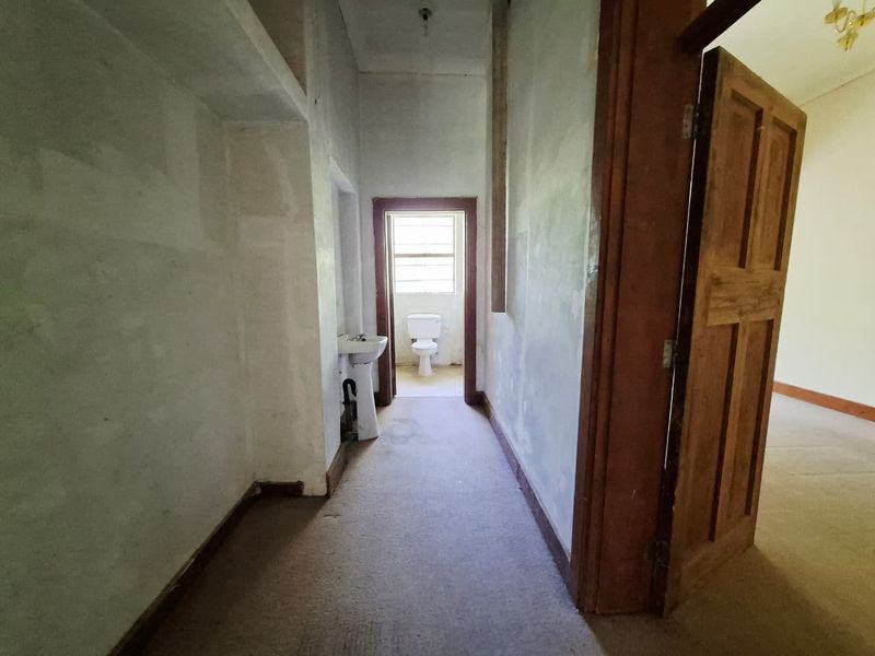 A vacant hallway leading to a small bathroom area featuring a pedestal sink and toilet, requiring cosmetic updates to wall finishes and flooring.