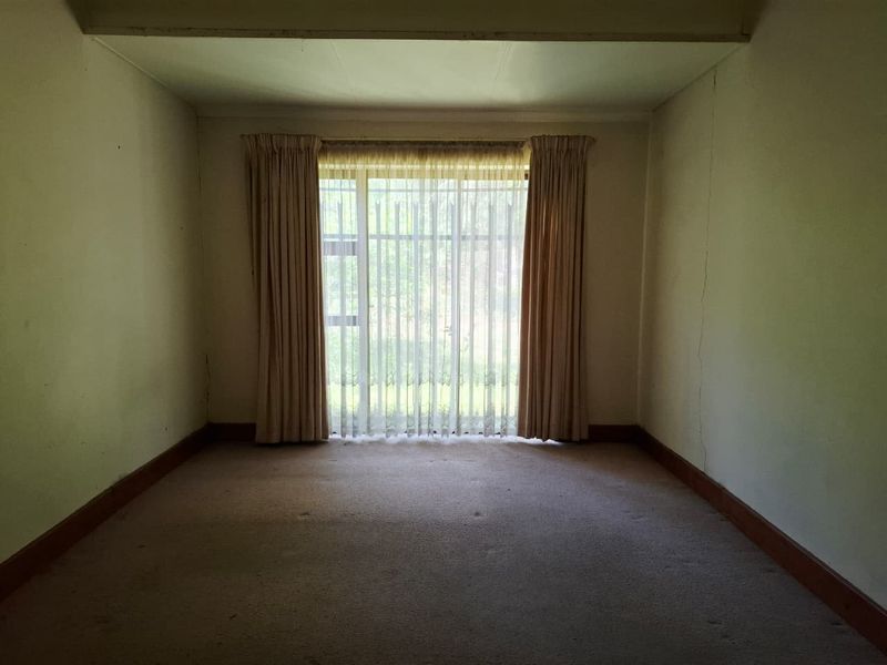 An empty living room featuring large windows, carpet flooring, and visible wall cracks, offering a blank canvas for renovation and modernization.
