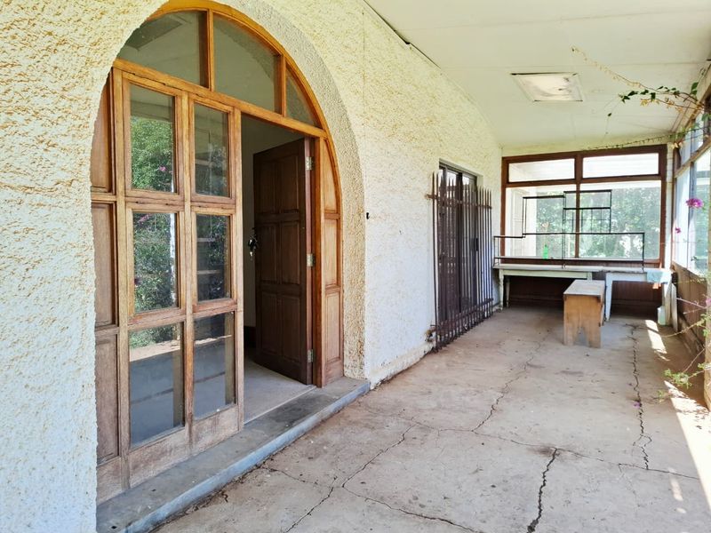 A covered patio area featuring an arched wooden entrance, concrete flooring with visible cracking, and integrated security features.