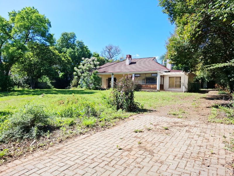 A single-story residential property featuring a tiled roof, brick chimney, and a covered porch, set on a large plot with a paved driveway.