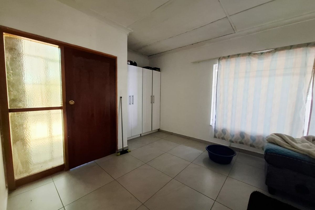 A bedroom featuring tiled flooring, built-in cupboards, and a timber entrance door with a glass side panel.