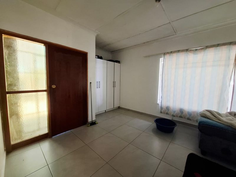A bedroom featuring tiled flooring, built-in cupboards, and a timber entrance door with a glass side panel.