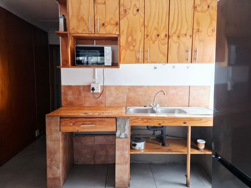 A functional kitchen featuring wooden cabinetry, a double bowl sink, and tiled splashbacks, currently showing signs of wear and unfinished construction details.