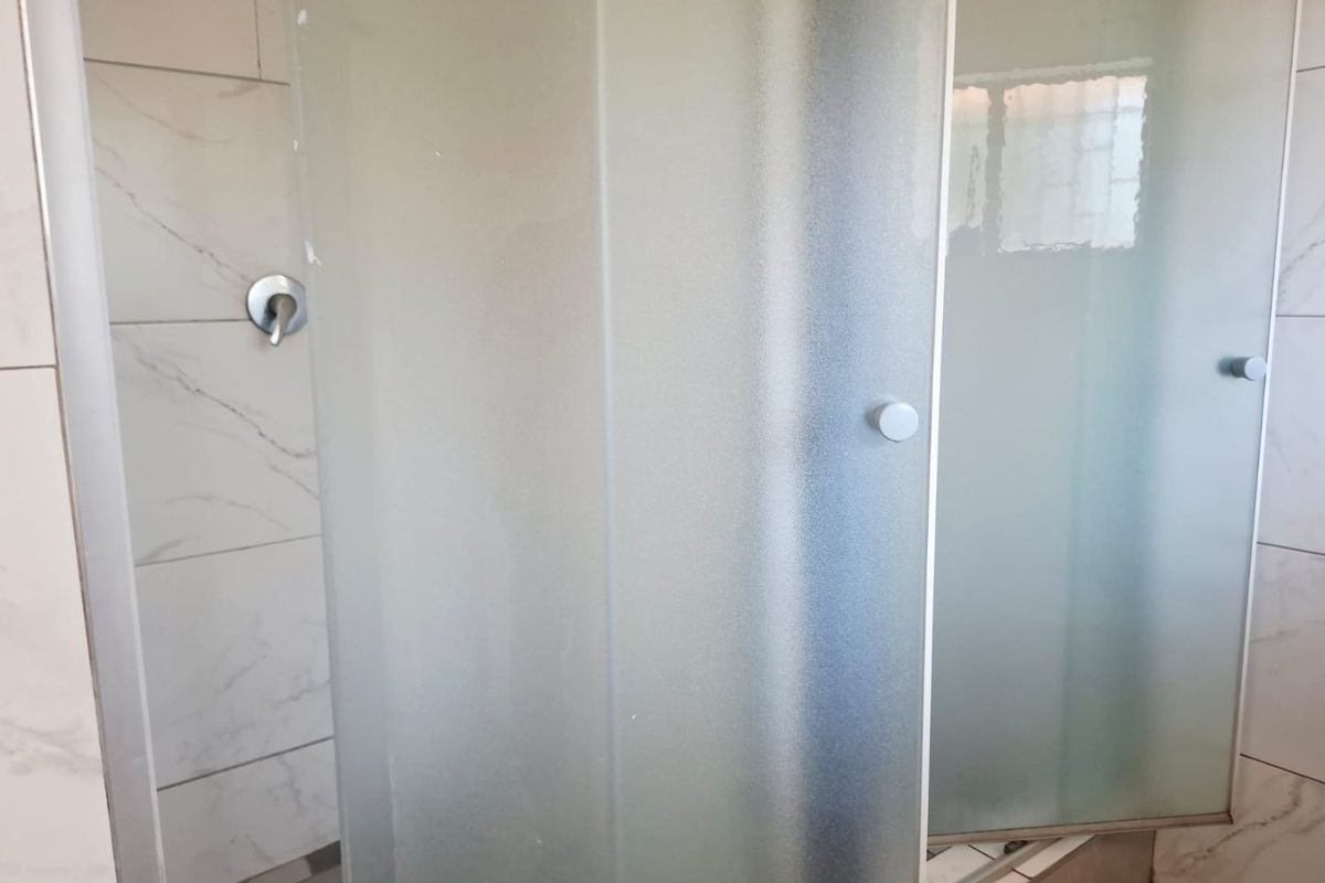 A clean bathroom shower area featuring a frosted glass enclosure, modern marble-look wall tiling, and mosaic floor tiles.