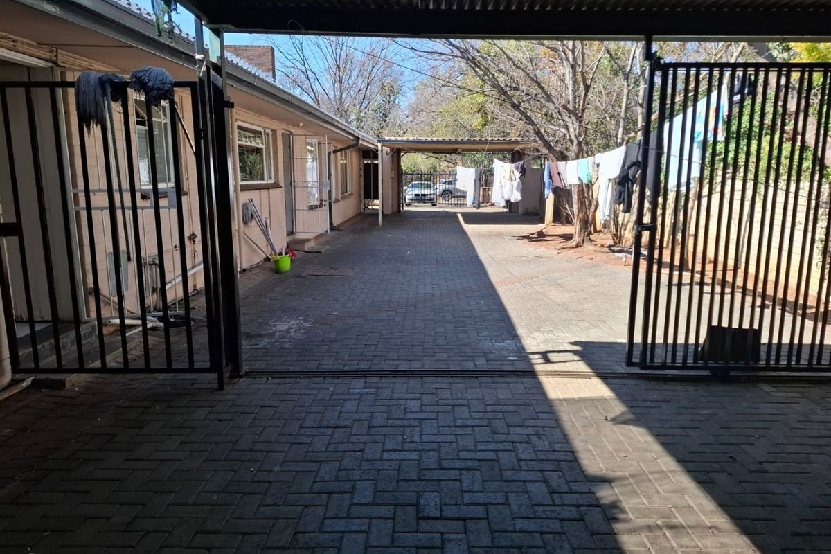 A paved rear driveway area featuring a metal security gate and covered parking structure.