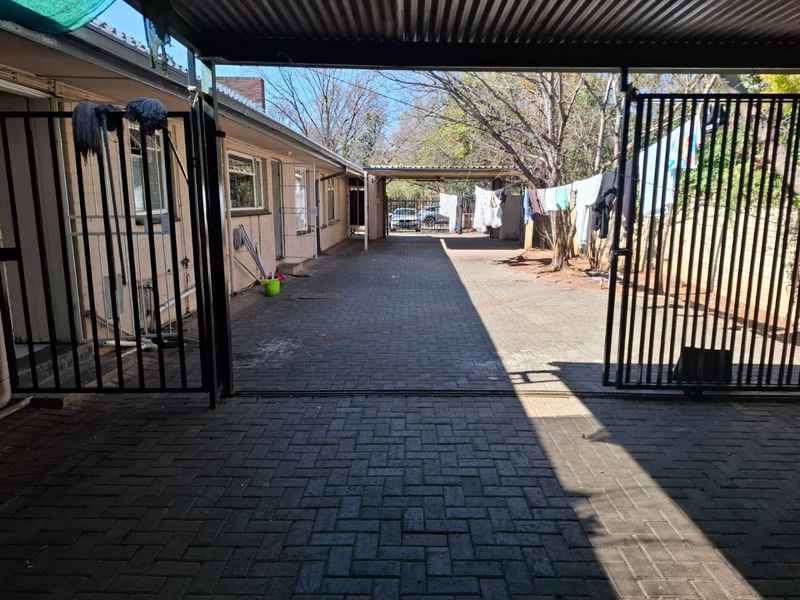 A paved rear driveway area featuring a metal security gate and covered parking structure.