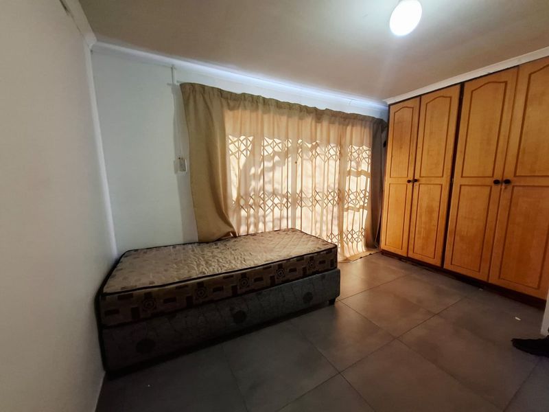A bedroom featuring tiled flooring, a built-in wooden wardrobe, and a security gate over the window.