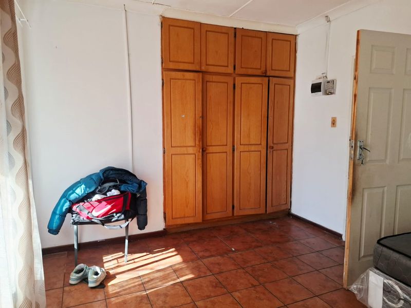 A bedroom featuring built-in wooden cupboards and tiled flooring, offering a functional space ready for cosmetic updates and modernization.