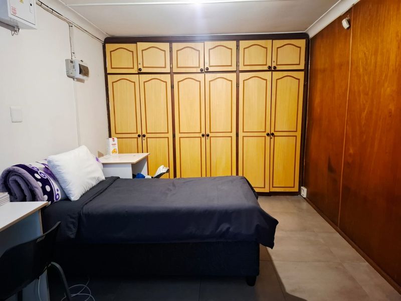 A bedroom featuring extensive built-in wooden cupboards, tiled flooring, and coving, offering functional storage space with a dated aesthetic.