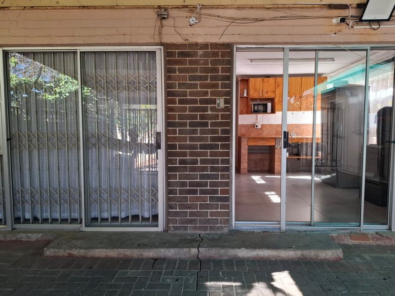 Covered patio area featuring sliding glass doors with security gates, providing access to an interior kitchen space with built-in cabinetry.