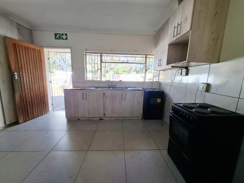 A functional kitchen space featuring tiled flooring, built-in cabinetry, and a double sink, with direct access to the exterior via a security gate.