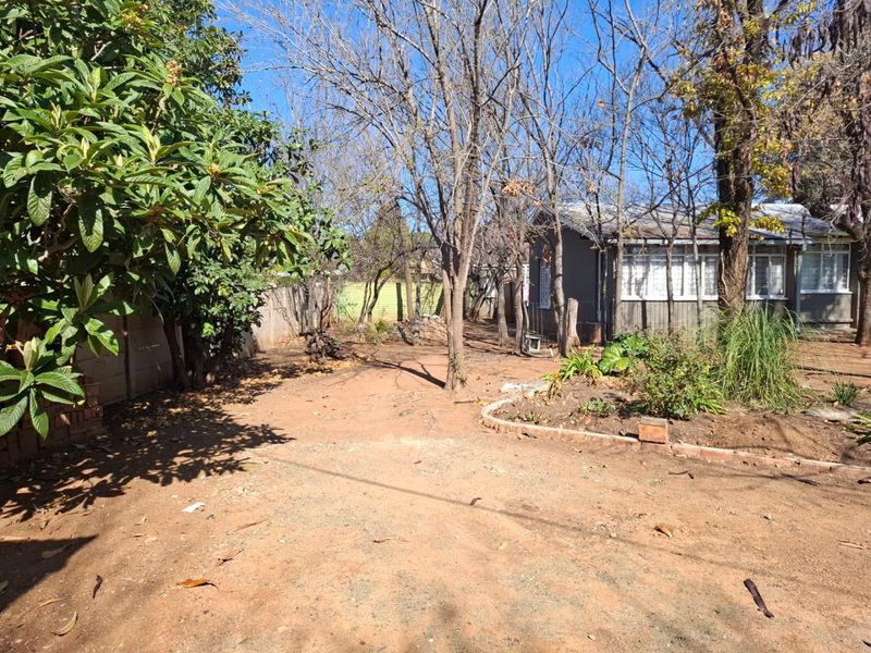 A spacious rear garden area featuring mature trees, brick garden edging, and a precast concrete boundary wall, offering potential for landscaping.
