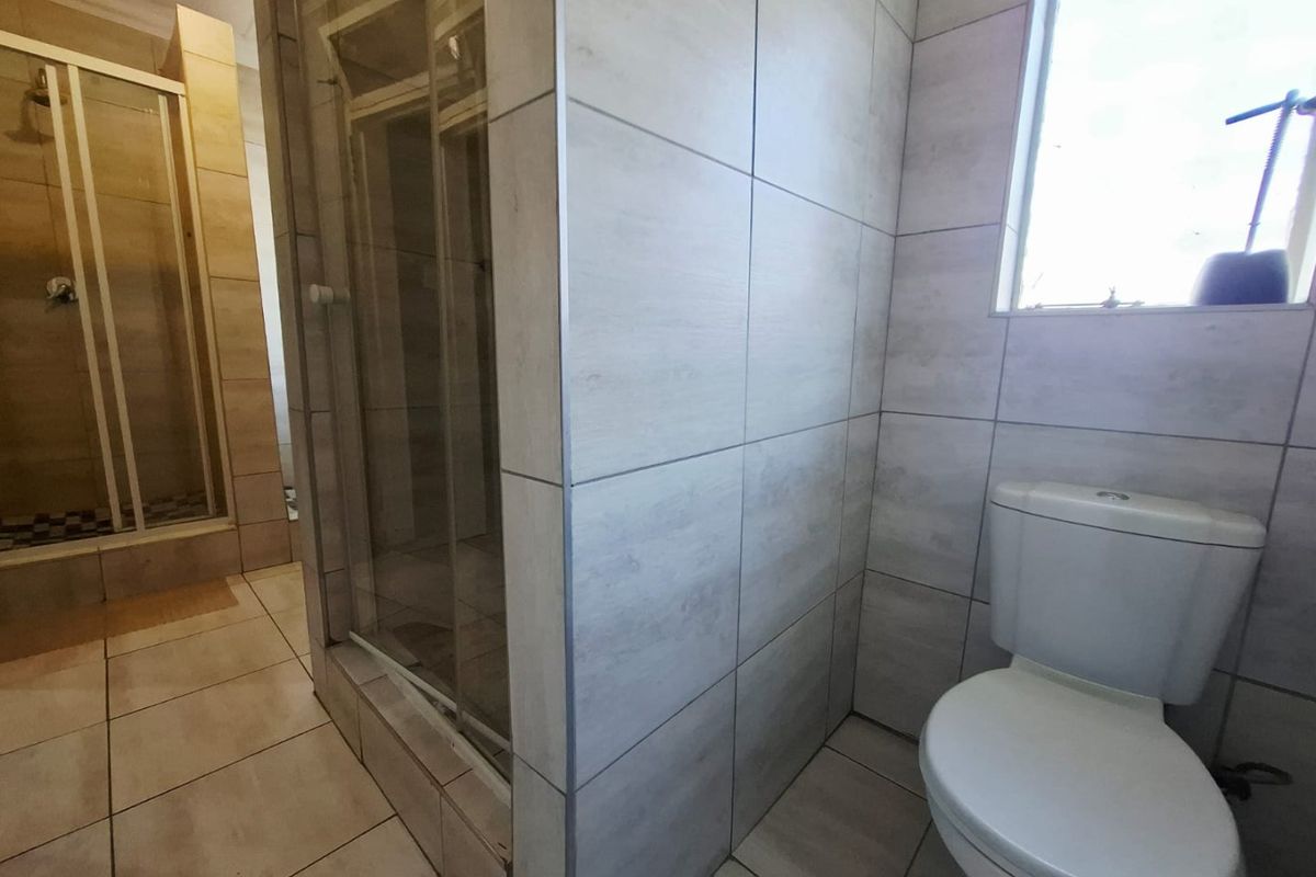 A clean, functional bathroom featuring a glass-enclosed shower, modern light-toned wall tiles, and a standard toilet.