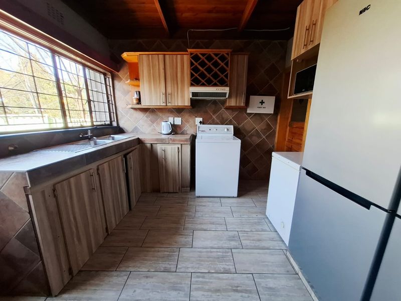 Functional kitchen featuring wood-look cabinetry, tiled backsplash, double basin sink, and exposed timber ceiling beams with ample natural light.