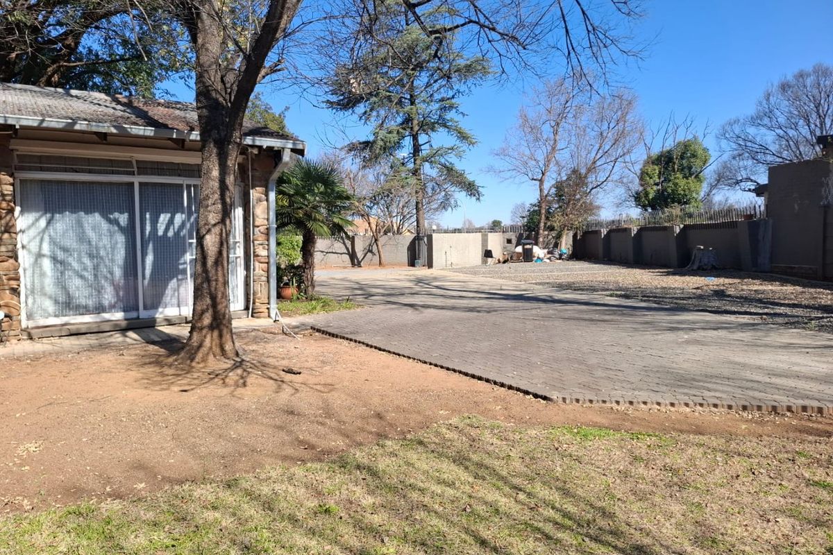 A spacious rear exterior area featuring a large paved driveway, perimeter walling, and direct access to the house via sliding glass doors.