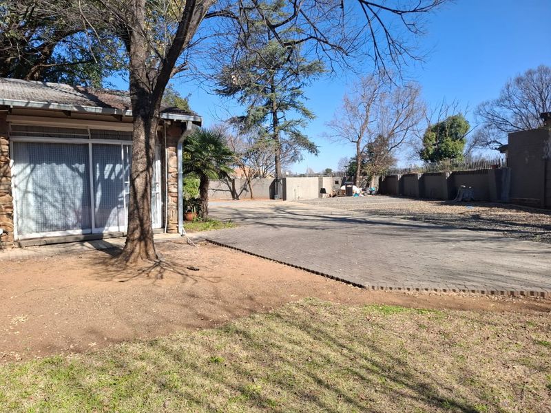 A spacious rear exterior area featuring a large paved driveway, perimeter walling, and direct access to the house via sliding glass doors.