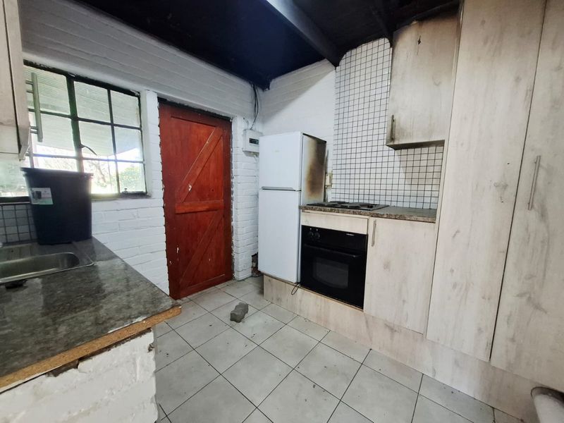 A compact kitchen featuring built-in cabinetry, a hob, oven, and tiled splashback, currently showing significant signs of wear and fire damage.