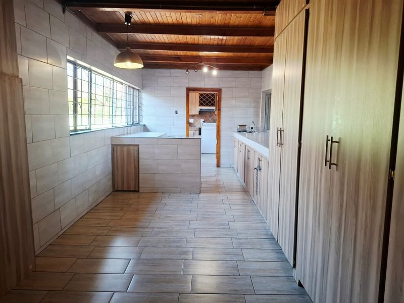 A spacious, modern kitchen featuring tiled walls and floors, extensive built-in cabinetry, and exposed timber ceiling beams, offering a clean and functional layout.