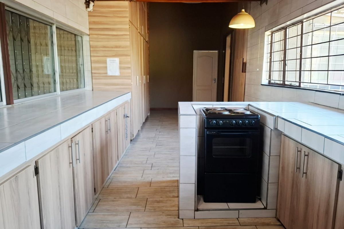 A functional kitchen featuring tiled countertops, built-in cabinetry, a freestanding stove, and tiled flooring with exposed timber ceiling beams.