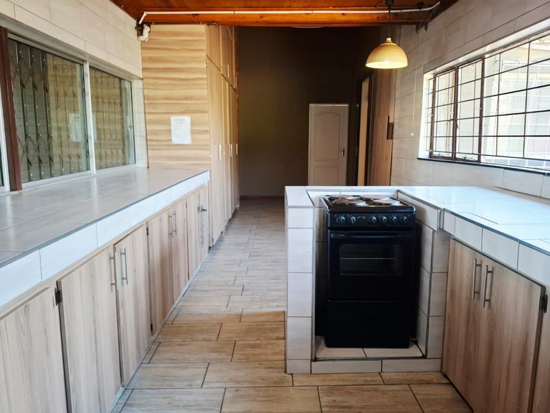 A functional kitchen featuring tiled countertops, built-in cabinetry, a freestanding stove, and tiled flooring with exposed timber ceiling beams.