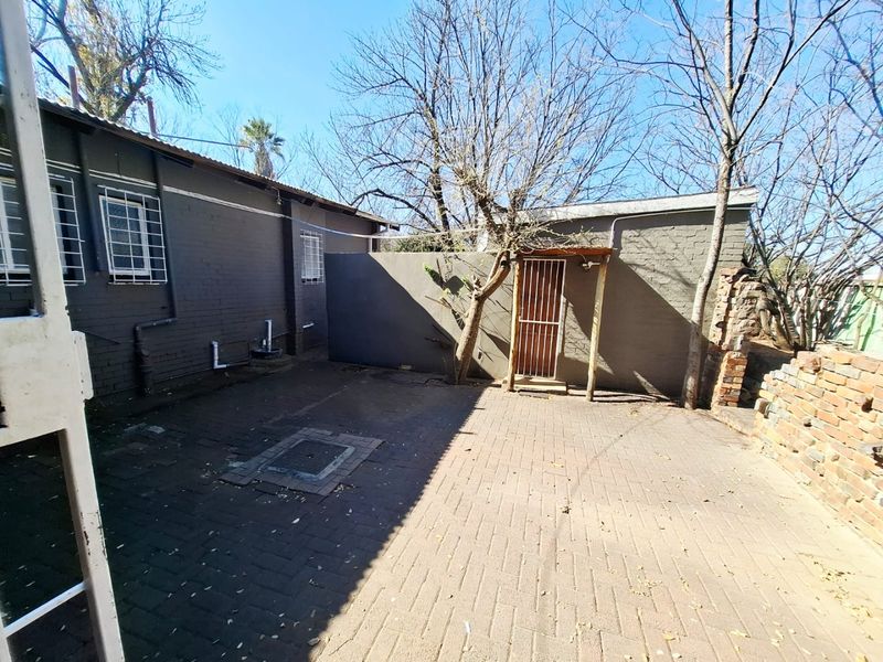 A rear courtyard area featuring paved flooring, security-fitted windows, and a brick boundary wall requiring some maintenance.