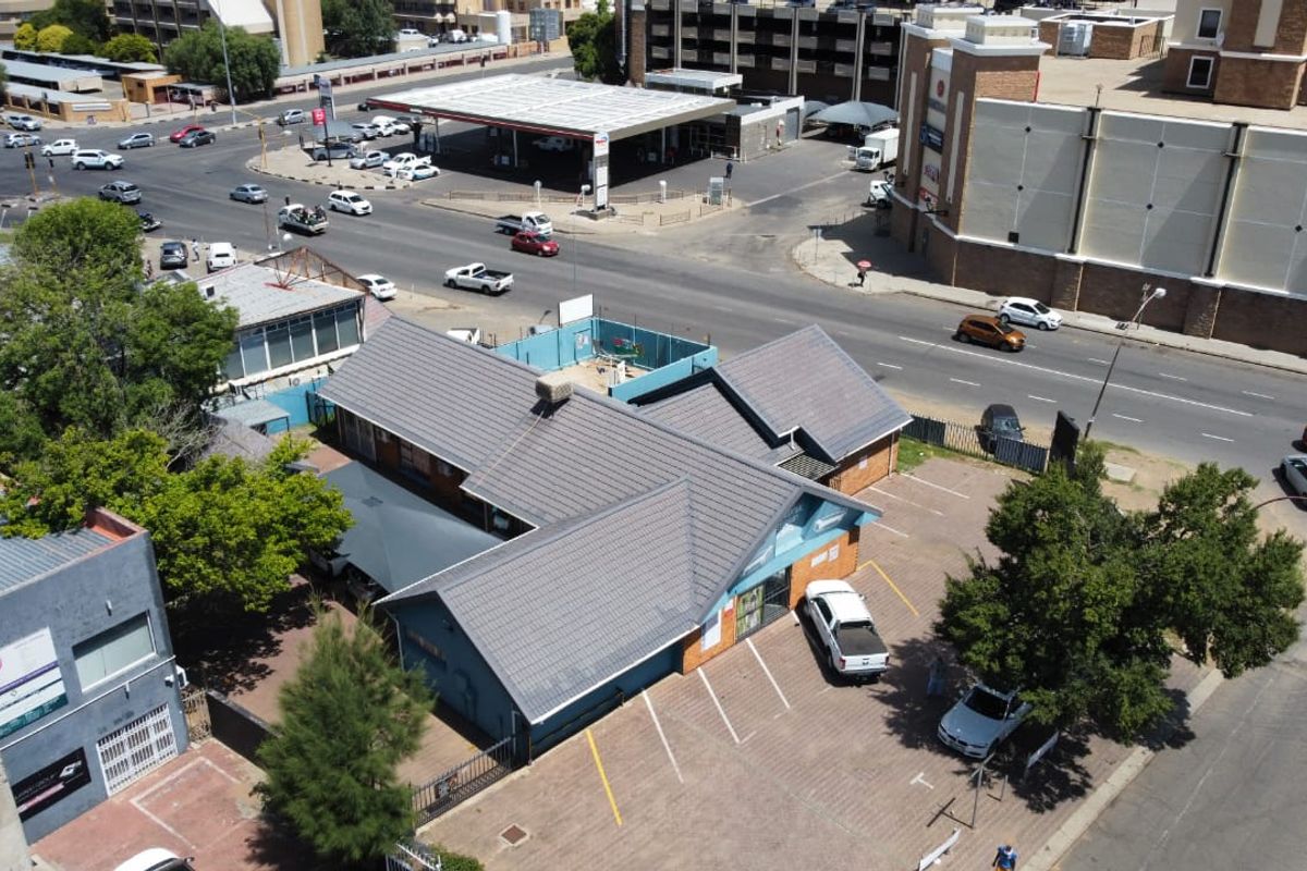 Aerial view of a commercial property featuring a tiled roof building with an adjacent paved parking area, situated in a busy urban street location.